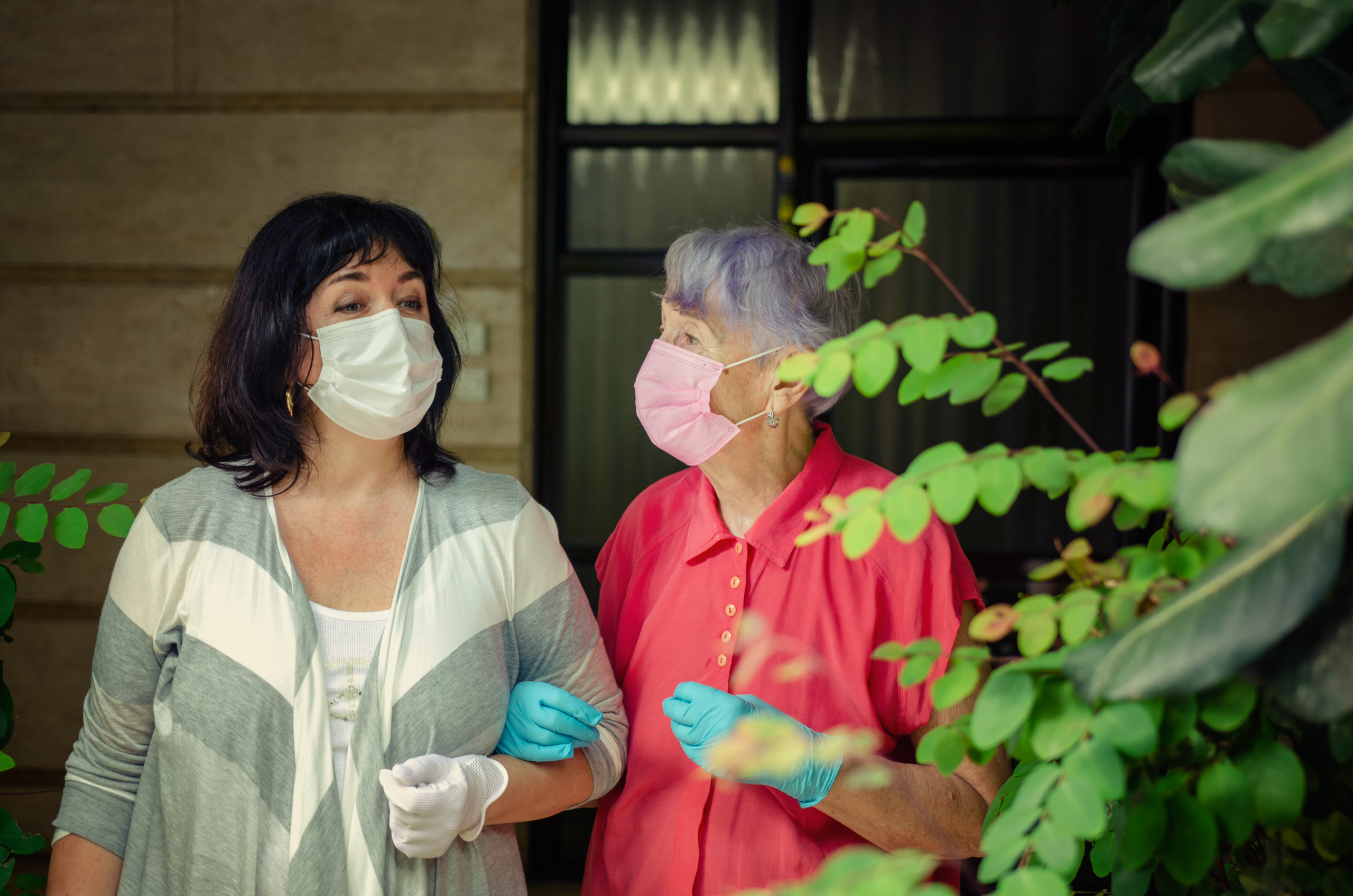 A caregiver took an elderly client out for a walk. Both wear protective face masks.