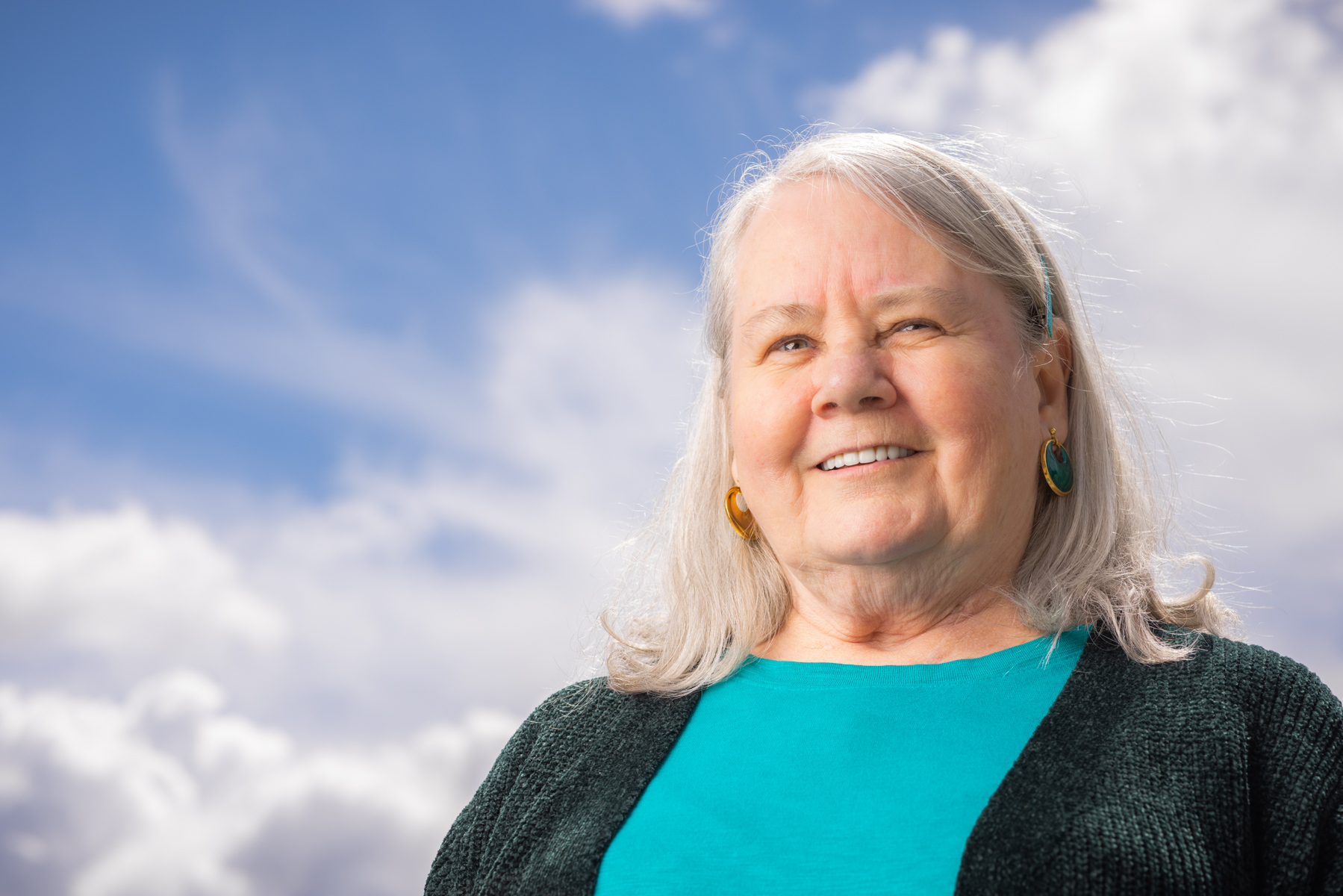 Lucille, woman smiling, looking into the distance with the sky in the background,