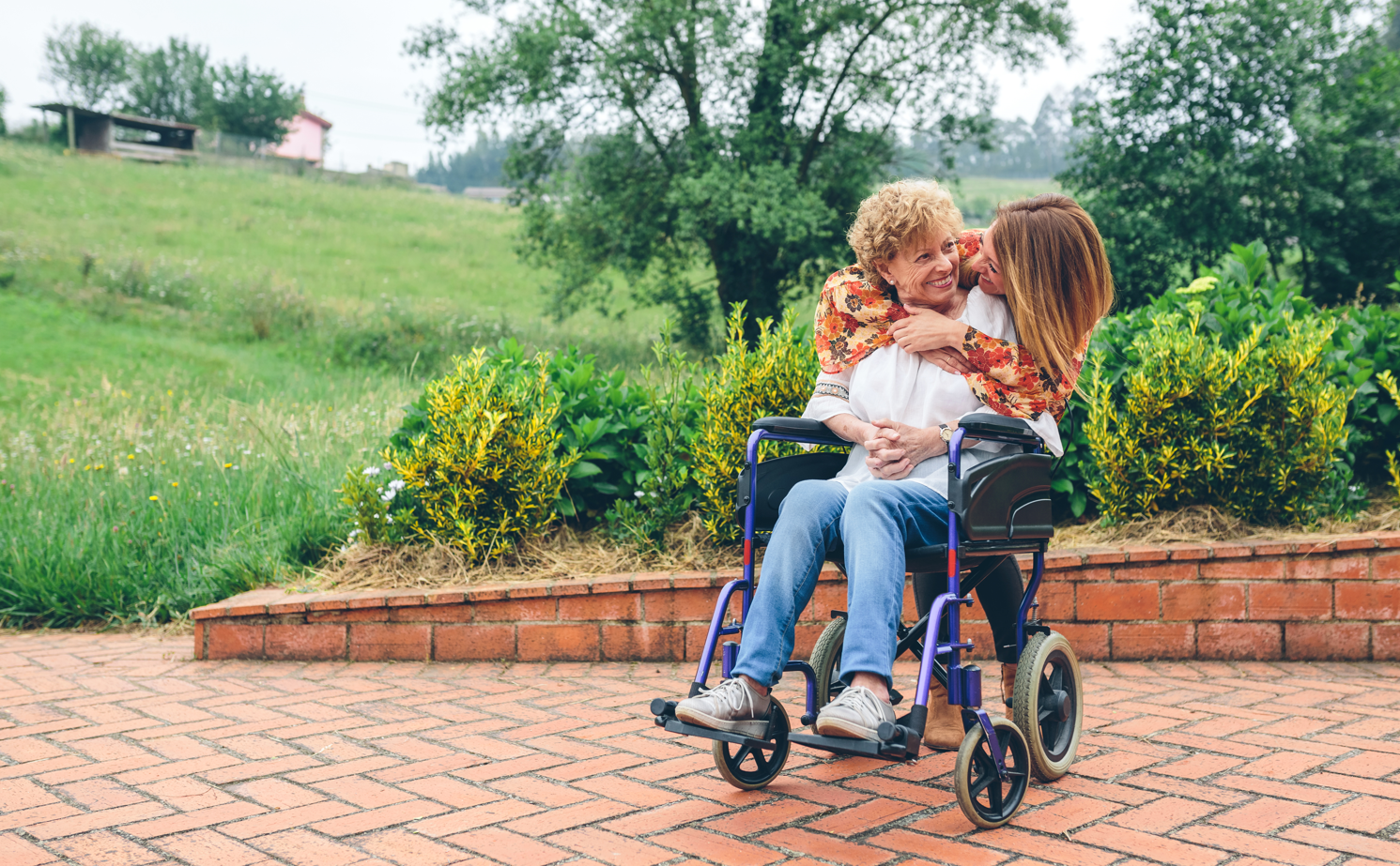 Daughter hugging her senior mother in wheelchair in the garden